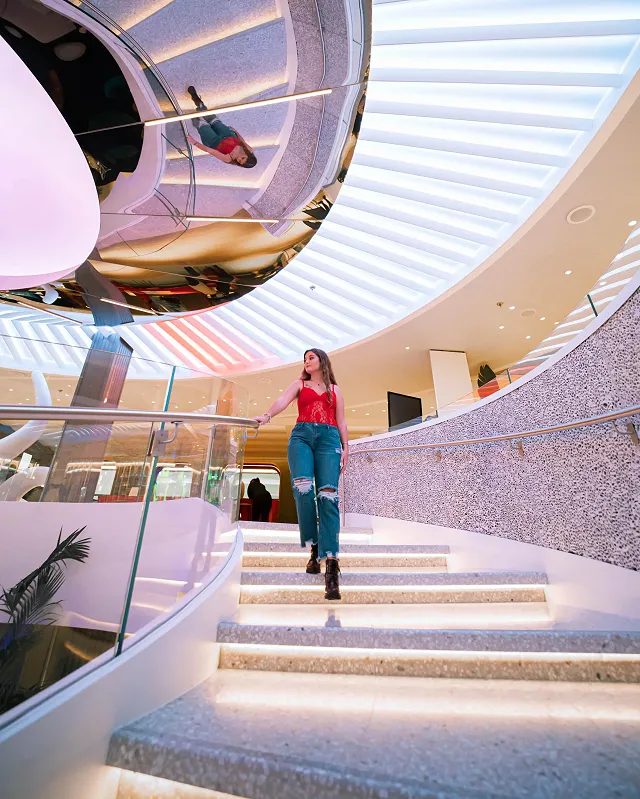 a girl walking down a spiral staircase on a virgin voyages ship